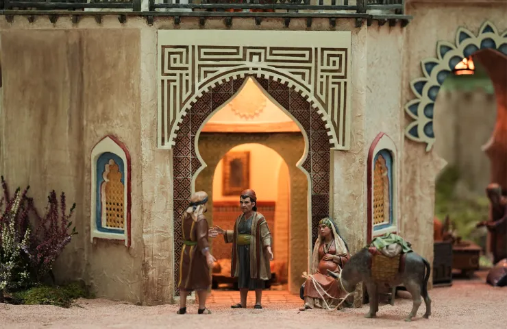escena de belén, puerta de arquitectura árabe, dos hombres hablando, mujer embazada sentada en el suelo, sujeta las riendas de un burro