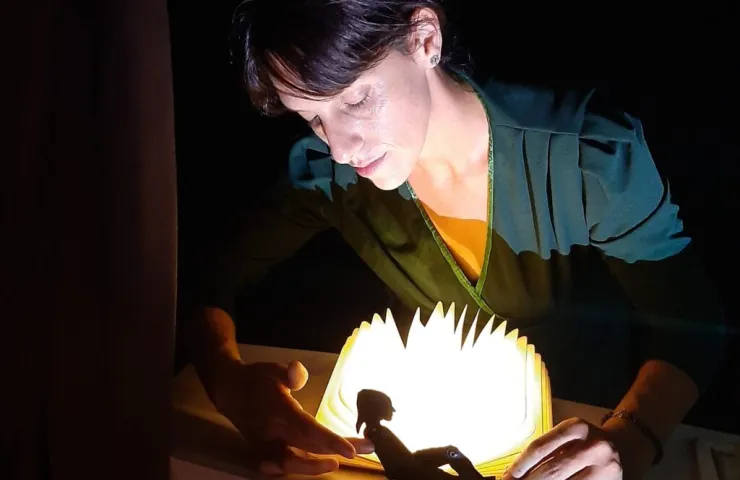 mujer con luz sobre una mesa sostiene en las manos una pequeña muñeca  negra