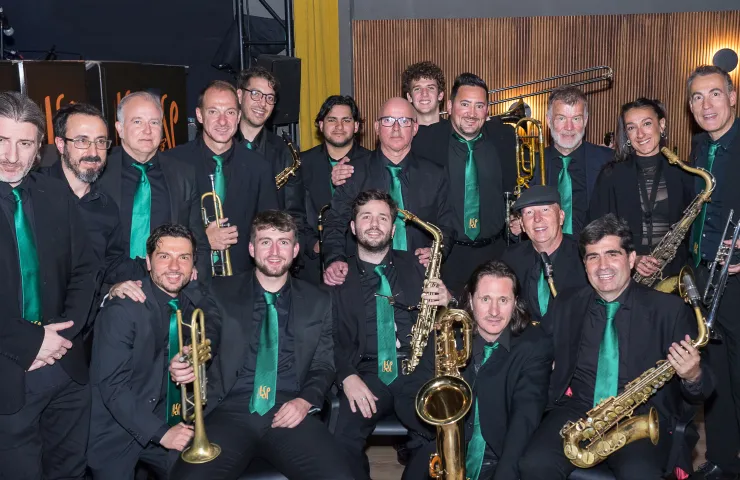 foto de los componentes de la bandea posando de frente vestidos con camisas negras y corbatas verdes, instrumentos de viento en las manos