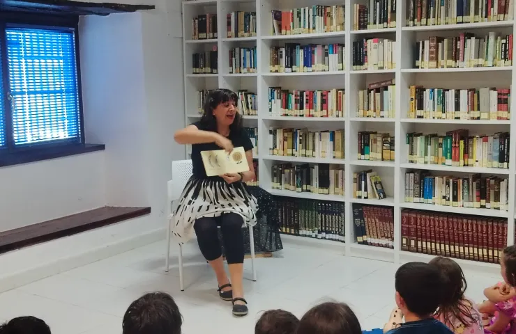 mujer sentada contando un cuento a unos niños en una bilblioteca