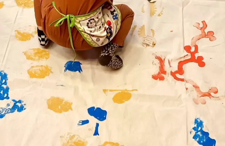 suelo con tela con manchas de pintura, niño descalzo encima al que solo se le ven los pies y un poco la espalda