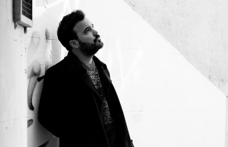 Foto en blanco y negro de un hombre apoyado en una pared, con actitud pensativa y mirando hacia arriba.