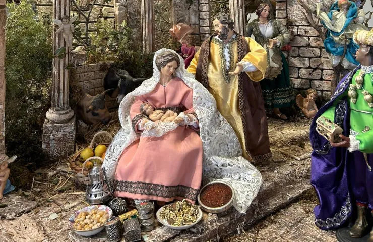 figura del belén con manto sobre la cabeza y los hombros sentada con platos de alimentos sobre las manos y alrededor